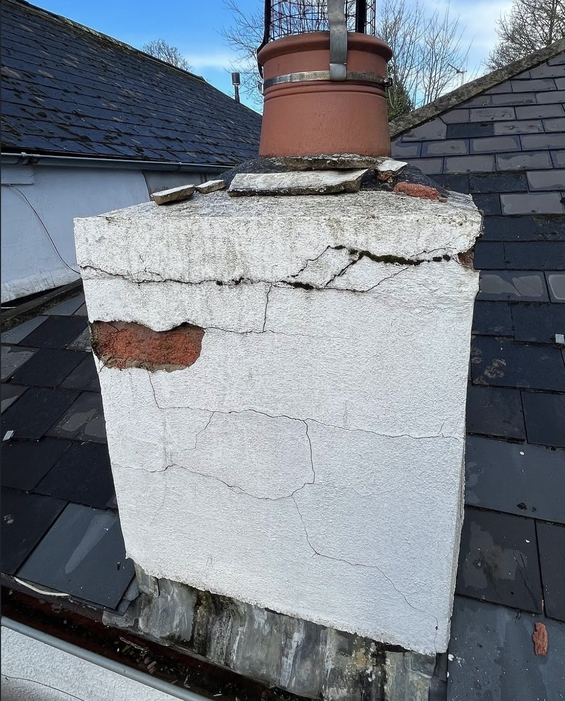 Cracked and spalled rendered chimney stack with damaged flaunching