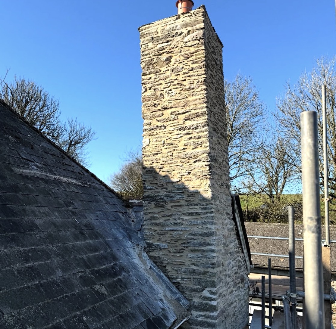 Tall natural stone chimney stack rebuilt above a slate roof